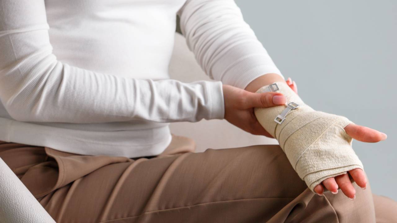 Κοντινό πλάνο ατόμου με νάρθηκα για σύνδρομο καρπιαίου σωλήνα, καθισμένο με χέρια στα πόδια